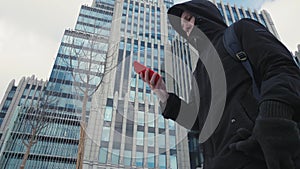 Man in black jacket and backpack using mobile phone and walking on city street