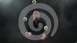 Man in black juggling white balls. Concentration, control and ability.
