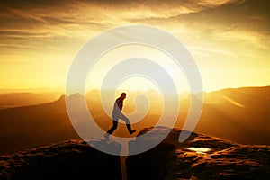 Man in black jumping between peaks. Dreamy daybreak