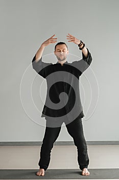 A man in black kimano practicing qigong energy exercises indoors