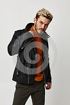 man in black leather jacket and orange sweater blond light background cropped view
