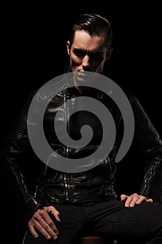 Man in black leather jacket posing seated in dark studio