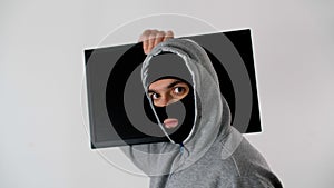 Man in a black mask and a hood is trying to take the TV imperceptibly past the camera.