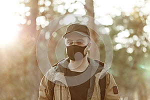 Man in black medical mask and in cap posing on the camera on trees background.