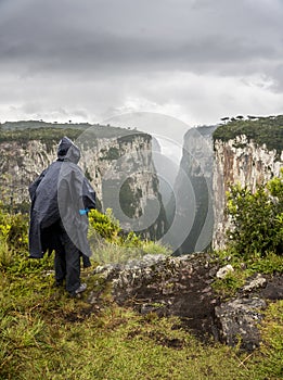 Man in black raincoat and hood standing on the edge of a cliff before rain, canyon itambezinho