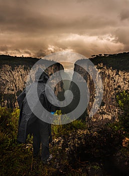 Man in black raincoat and hood standing on the edge of a cliff at sunset