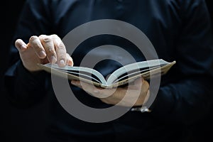 A man with a black robe holds a book in front of him and tries to turn the page