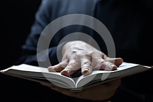 A man black robe put his hand palm on a book
