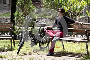 Man on park bench sitting next to electric bicycle