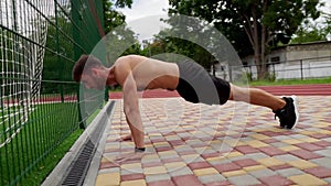 Man in black shorts, shirtless doing push ups on paved ground outdoors