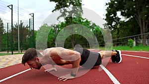 Man in black shorts, shirtless doing push ups on race track stadium outdoors