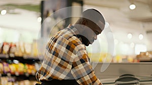 a man with Black skin color in a plaid shirt inspects refrigerators in a supermarket