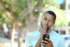 Man with black sking holding phone and thinking