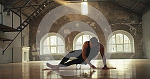 A man in a black sports summer uniform stretches his leg muscles with a special fitness cone in a sports brick hall