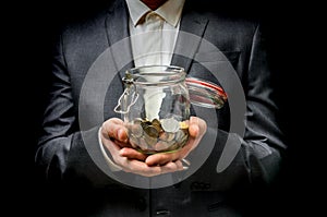 Man in black suit holding money jar with coins