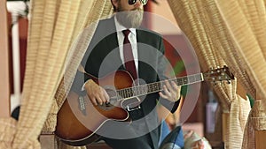 Man in black suit plays guitar sensually among curtains