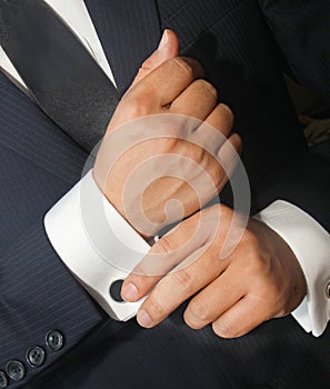 A man in a black suit straightens his cufflinks