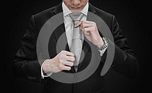 A man in black suit tying gray necktie on black background