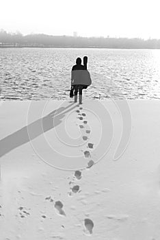 Man in black with suitcase and guitar walking towards water in winter season