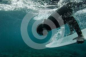 Man in the black swimsuit holding a surf board dive under the wave