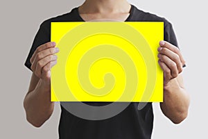 Man in black t shirt holding blank yellow A4 paper horizontally.