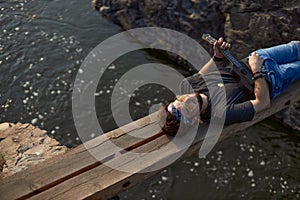 a man in a black T-shirt lies on a wooden bridge over a mountain river