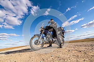 Man in a black uniform on bike against the backdrop of panorama of field and blue sky. motorcycle travel concept