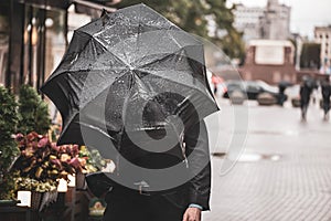 A man with a black wet umbrella was caught in a gust of wind on the street of the old city