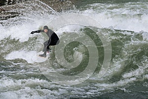 Man in black wetsuit surfing On Eisbach River Germany, Munich, Englischer Garden during winter