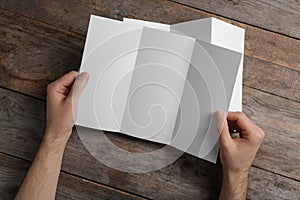 Man with blank brochure on wooden background, above view.