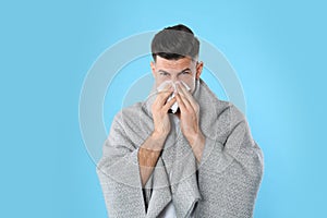Man with blanket suffering from runny nose on light blue
