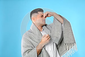 Man with blanket suffering from runny nose on light blue background