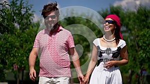 Man and blind woman are walking in park, holding hands, boyfriend is helping to girlfriend