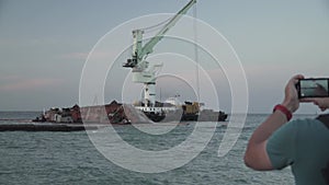 Man blogger records video blog on mobile phone for social media about accident of wreck tanker Delfi with oil in Odessa