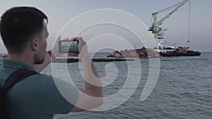 Man blogger records video blog on mobile phone for social media about accident of wreck tanker Delfi with oil in Odessa