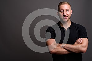 Man with blond hair wearing black polo shirt against gray backgr