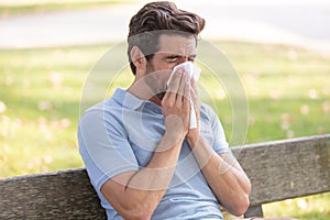 man blowing nose on tissue against peaceful autumn scene