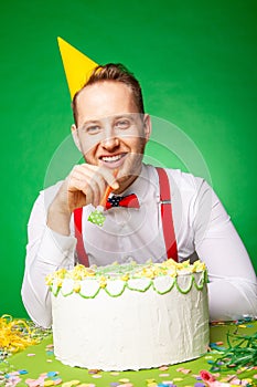 Man blowing party horn at table with birthday cake