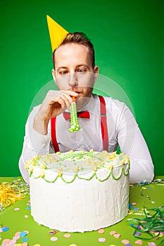 Man blowing party horn at table with birthday cake