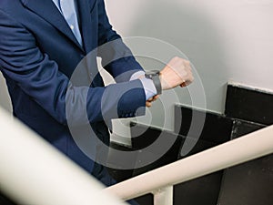 Man in blue blazer jacket walking upstairs checking the time on his watch