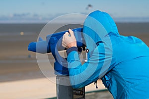 Man in blue coat looking on sea using coin operated binocular viewe