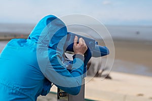 Man in blue coat looking on sea using coin operated binocular viewe