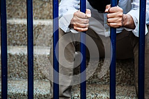 A man in blue collar shirt and black slacks behind the iron fence, Hand holding iron fence with a sense of hopelessness, sadness