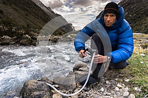 Man in blue down jacket filtering drinking water from a mountain river in Peru