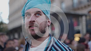 Man with blue eyes and a scarf on his head looks upwards