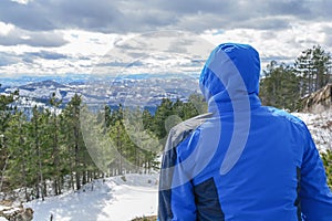 Man with blue jacked sitting and looking on valley and pine tree