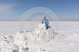Man in a blue jacket building an igloo on a glade
