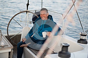 Man in blue jacket on the yacht having coffee and looking contented