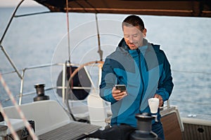 Man in blue jacket on the yacht having coffee and looking contented