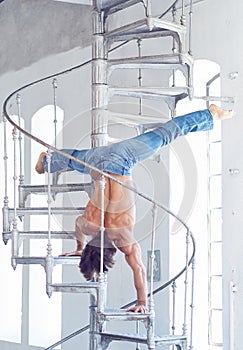 A man in blue jeans upside down on iron ladder.